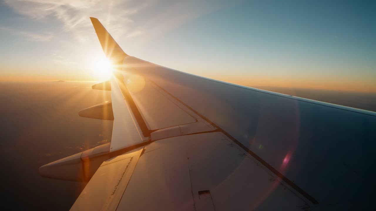 Reflecting airliner wing basking in sun descending behind wingtip at high altitude, with lens flare
