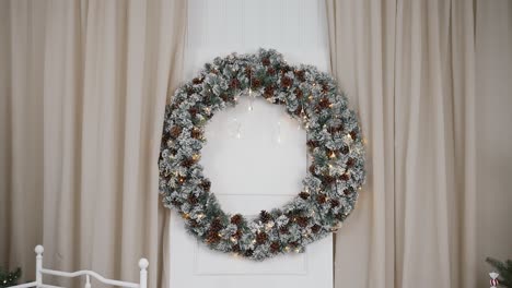 large snow-dusted pinecone wreath with twinkly lights on christmas set