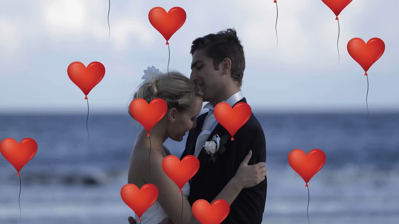 Muitos balões de coração flutuando contra um casal recém-casado se abraçando na praia.