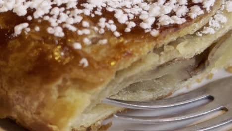 close-up of a golden brown, flaky puff pastry dessert, generously dusted with powdered sugar, near a fork, revealing the soft, airy interior, ready to be savored