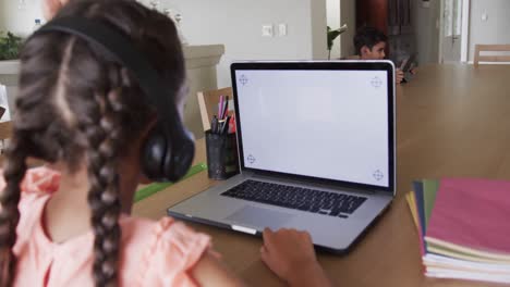 Chica-Birracial-Aprendiendo-En-Línea-En-La-Mesa-Usando-Una-Computadora-Portátil-Con-Espacio-Para-Copiar-En-La-Pantalla,-Cámara-Lenta