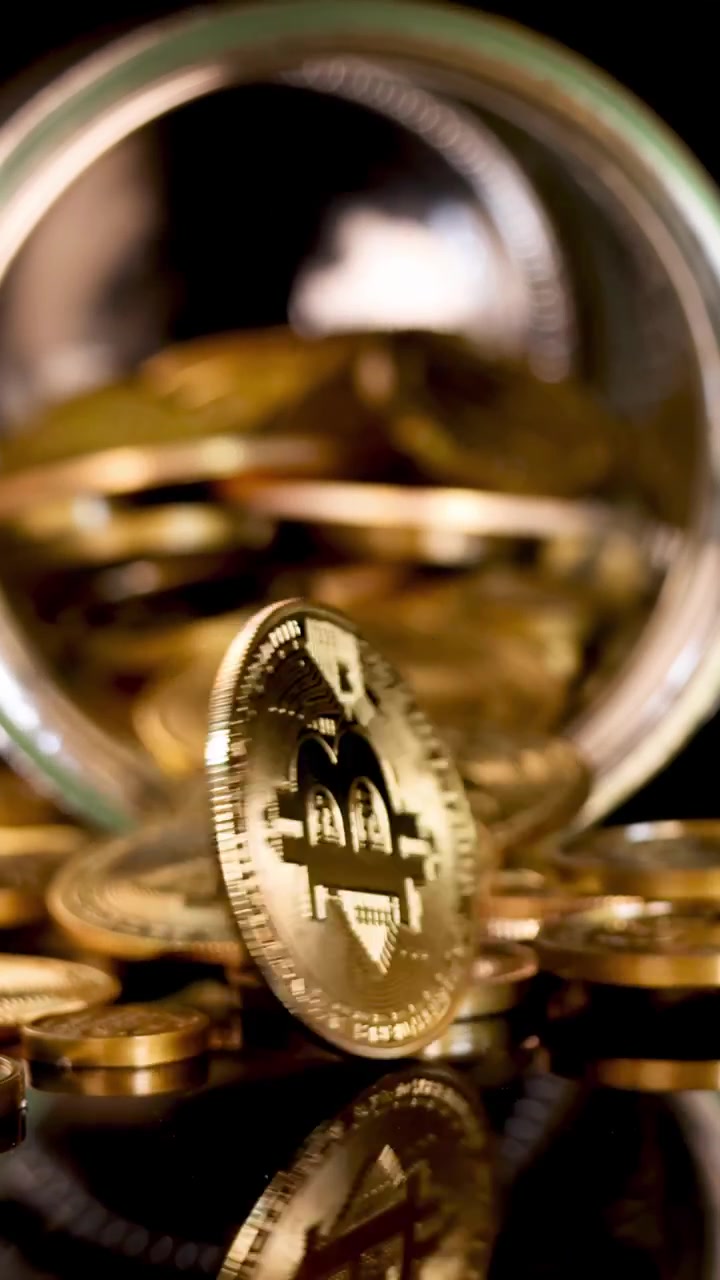Moeda de ouro gira e cai em uma superfície reflexiva, cercada por moedas derramando de um pote de vidro.