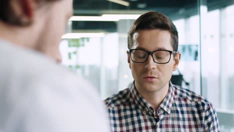 Rear-view-of-caucasian-male-doctor-sitting-at-desk-explaining-to-male-patient-treatment-for-coronavirus-in-medical-consultation