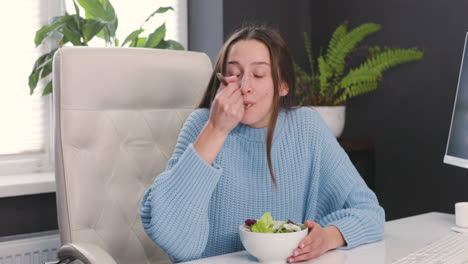 mujer sonriente sentada en el escritorio y comiendo ensalada saludable