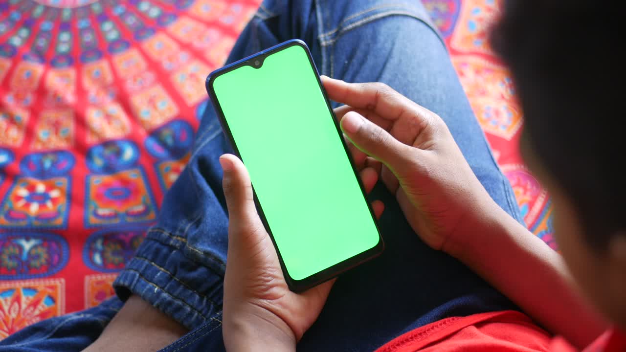 mano de un joven usando un teléfono inteligente con pantalla verde en la cama