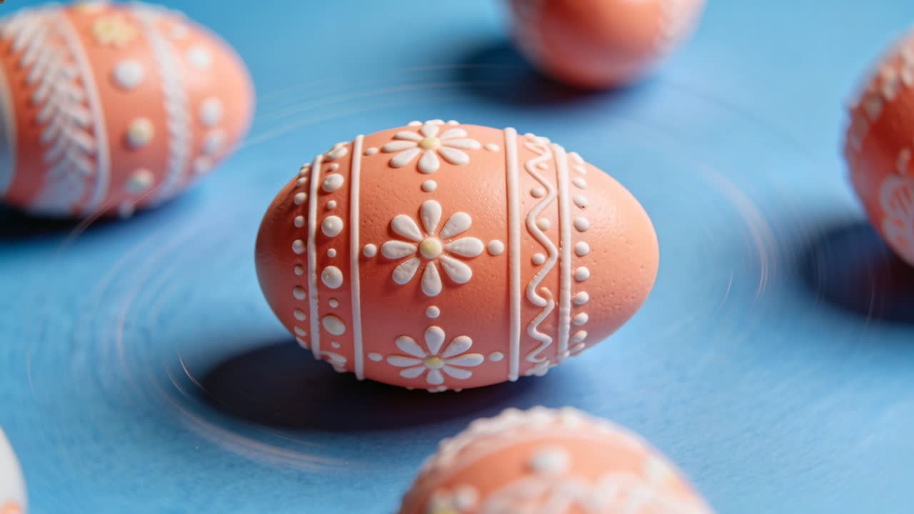 Rotating peach-pink egg revealing white piping on blue table as camera tightens, with motion rings