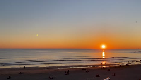 Increíble-Fondo-De-Gran-Puesta-De-Sol-Con-Algunas-Personas-Bañándose-En-El-Mar-Y-Algunos-Surfistas-Practicando-Paddle-Y-Algunas-Personas-Viendo-El-Paisaje-En-Cascais,-Portugal