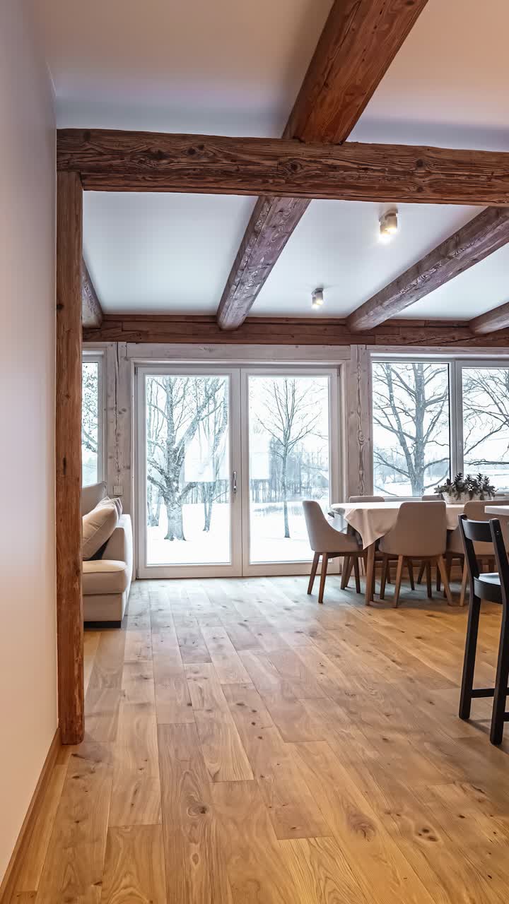 The beautiful interior design of a modern rustic kitchen and dining room in a Latvian log cabin, featuring exposed wooden beams, a large kitchen island, and a view of a snowy winter landscape