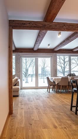 the beautiful interior design of a modern rustic kitchen and dining room in a latvian log cabin, featuring exposed wooden beams, a large kitchen island, and a view of a snowy winter landscape