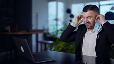 confident man at the desk in office putting on mask. businessman speaking and pointing at something. pandemic precautions concept.