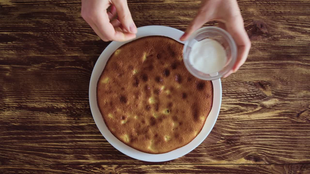manos de mujeres en una camisa azul a cuadros poner un plato de pastel de manzana en una vieja mesa rústica y salpicarlo con azúcar en polvo