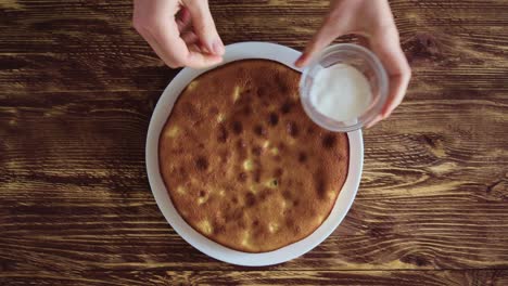 women's hands in a checkered blue shirt put a plate of apple pie on an old rustic table and sprinkle it with powdered sugar