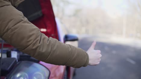 closeup hand of a man hitchhiking on a road with his broken down car close to him