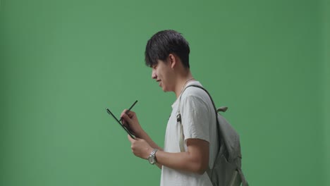 태블릿에 글을 쓰고 녹색 스크린 스튜디오에서 는 아시아 남성 학생의 측면 시각