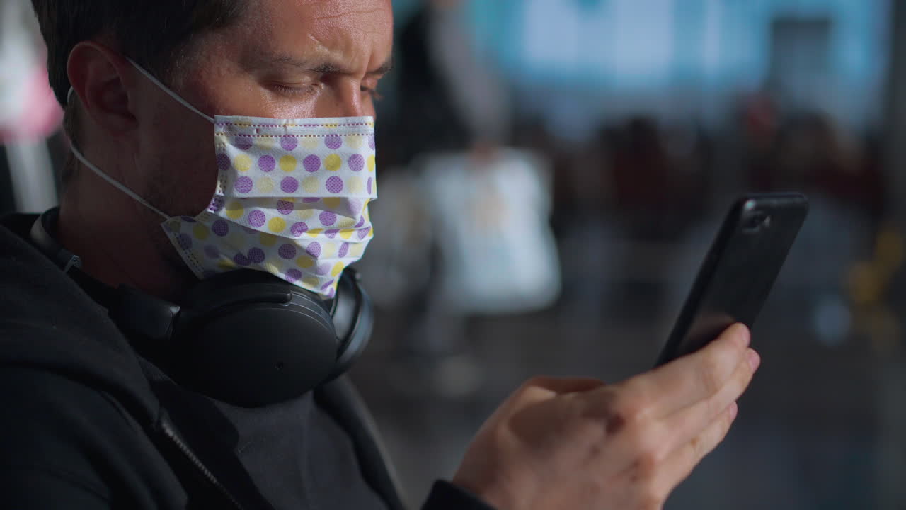 hombre con una máscara y usando un teléfono en el aeropuerto