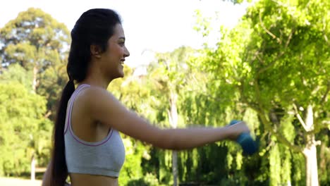 sonriente bruneta enfocada levantando pesas en el parque