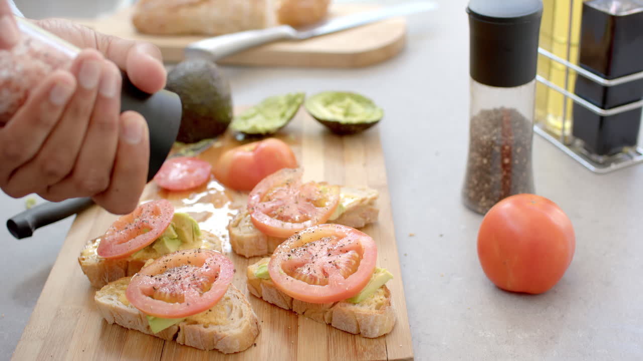 Seasoning avocado and tomato toast with pink salt on wooden cutting board