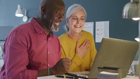 Happy-senior-diverse-couple-sitting-at-table-and-working