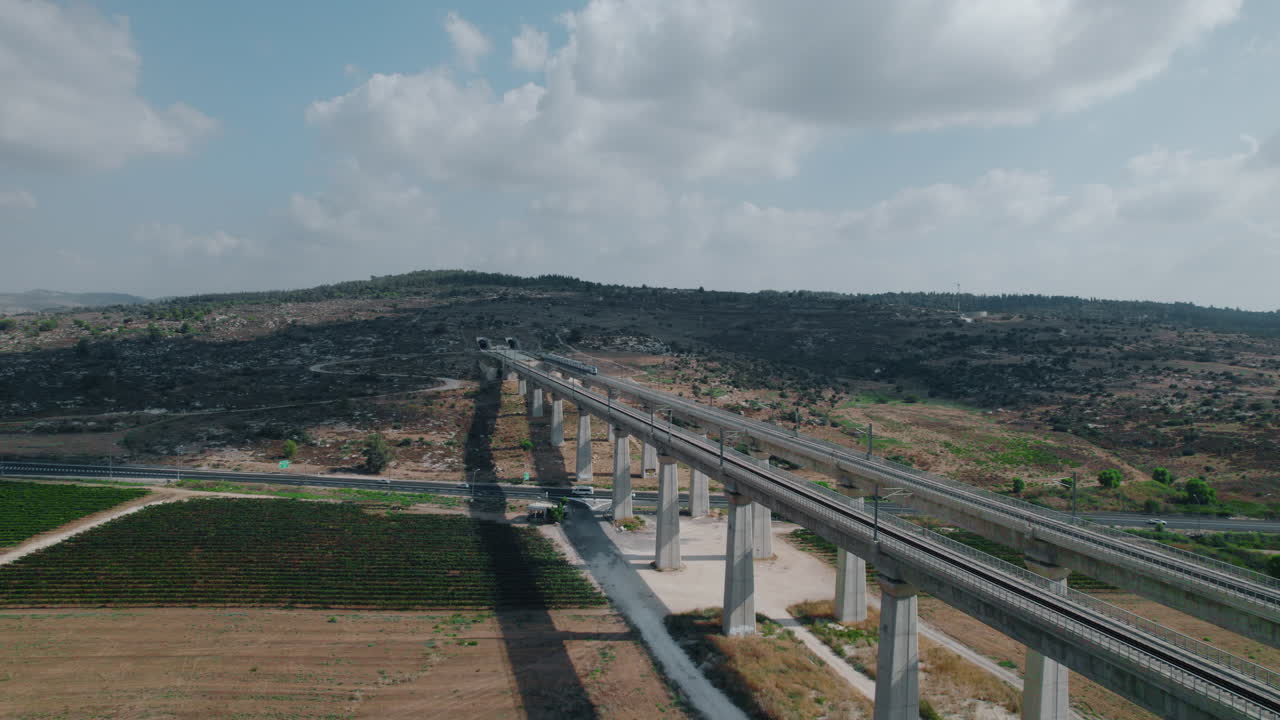 поезд покидает туннель, вырезанный в горах, и проходит через массивный железнодорожный мост через дорогу с машинами и сельскохозяйственными полями - воздушный параллакс