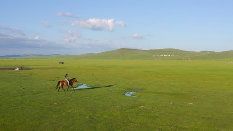 horsewoman riding horse through vast meadow valley in mongolia