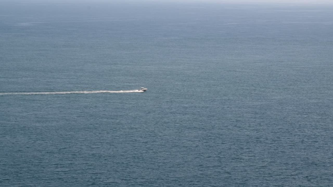 Locked-off wide shot of a speedboat cruising through calm blue ocean waters