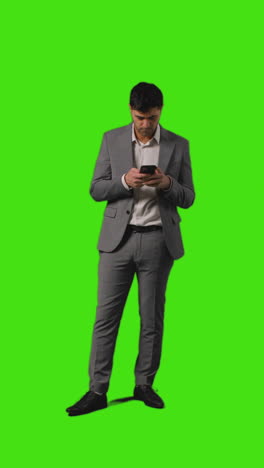 Vertical-Video-Of-Businessman-Sending-Text-Message-On-Mobile-Phone-Standing-Against-Green-Screen-Background