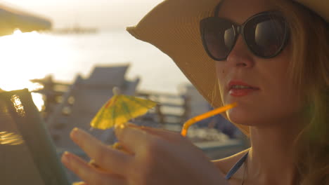 mujer con sombrero y gafas de sol bebiendo cóctel