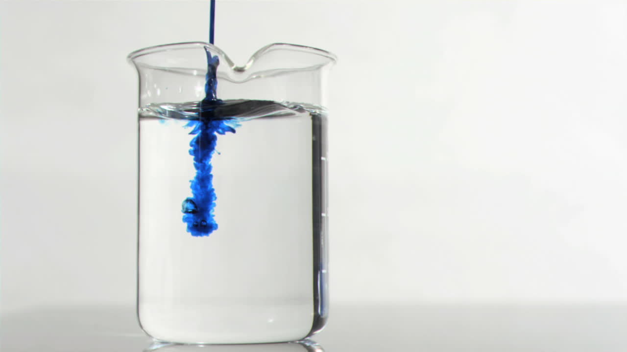 un fino goteo azul en un movimiento súper lento que fluye en un agua en un vaso