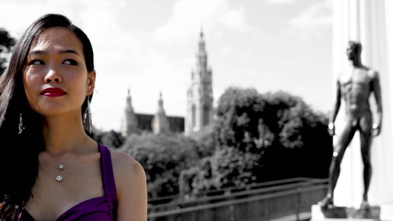 작은 아시아 소녀가 비엔나의 고전 건축물 앞에서 다른 방향으로 눈을 돌리고 있습니다.