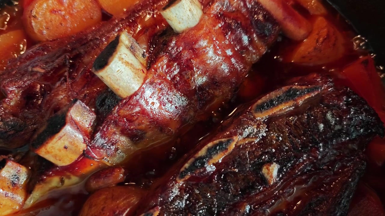 Vista dall'alto di costine di manzo Asado a cottura lenta in brodo ricco con patate, patate dolci e cipolla che bollono in una pentola nera. Stufato di carne gourmet rustico, primo piano di comfort food.