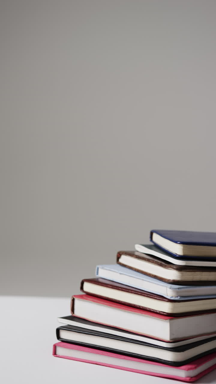 Vertical video of stack of books with copy space on grey background, in slow motion