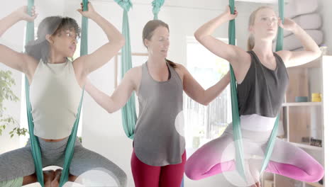 animation of light spots over diverse female instructor and teenage girls practicing aerial yoga