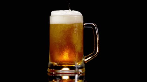 pouring lager beer into a beer mug with froth in black background - studio shot