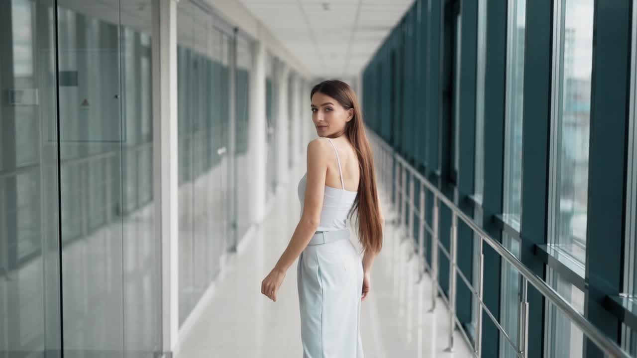 바지와 블라우스를 입은 세련된 성인 소녀는 긴 머리를 아름답게 발산합니다.