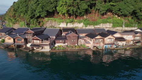 boat houses establishing shot in kyotango japan seaside village home valley green hills mountain background, drone aerial view ine town inecho