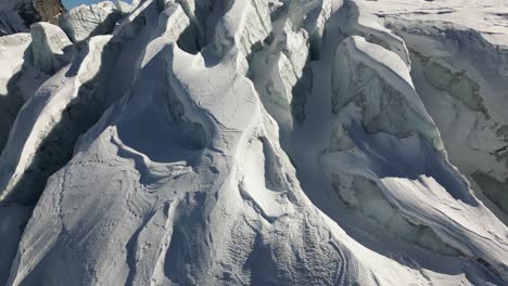 Aerial-tilt-up,-snow-covered-glacier-with-relief-in-the-Swiss-alps-in-winter