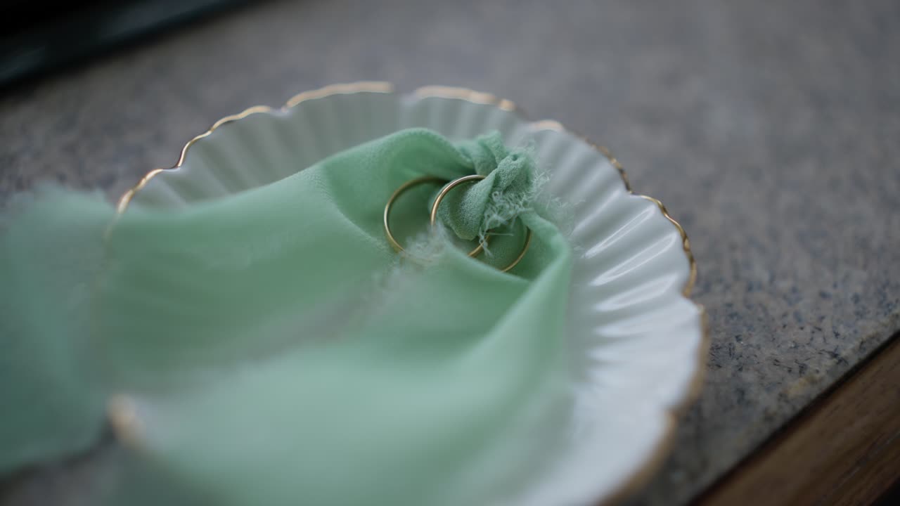 two wedding bands tied with green ribbon in a scalloped white ring tray