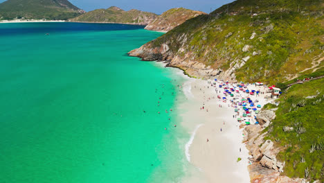 vista aérea de praia do pontal en arraial do cabo, brasil, nadadores en aguas azules claras y montañas de la isla en el fondo