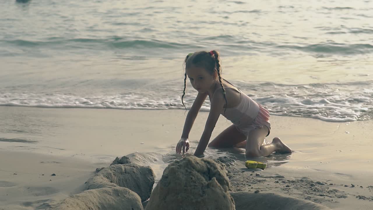 girl digs moat from sand castle to sea on beach slow motion