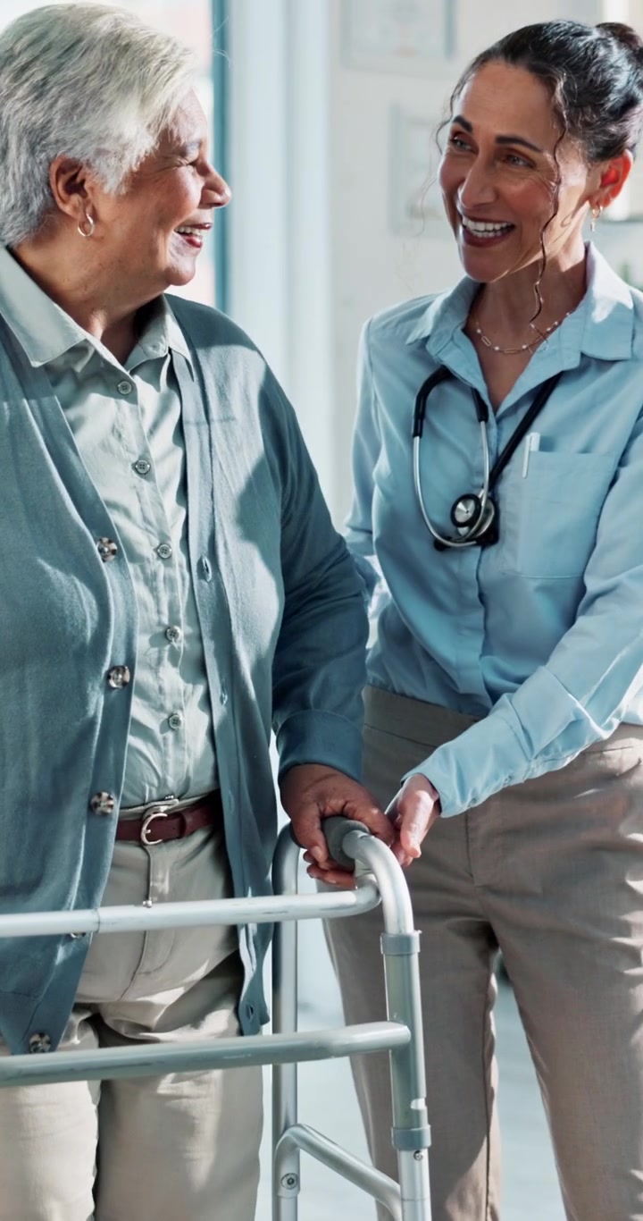 Kvinnelig Lege som Hjelper Eldre Kvinne med Rullator på Klinikk