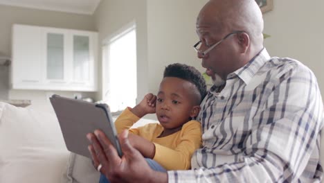 African-american-grandfather-with-grandson-using-tablet-on-couch-at-home,-slow-motion