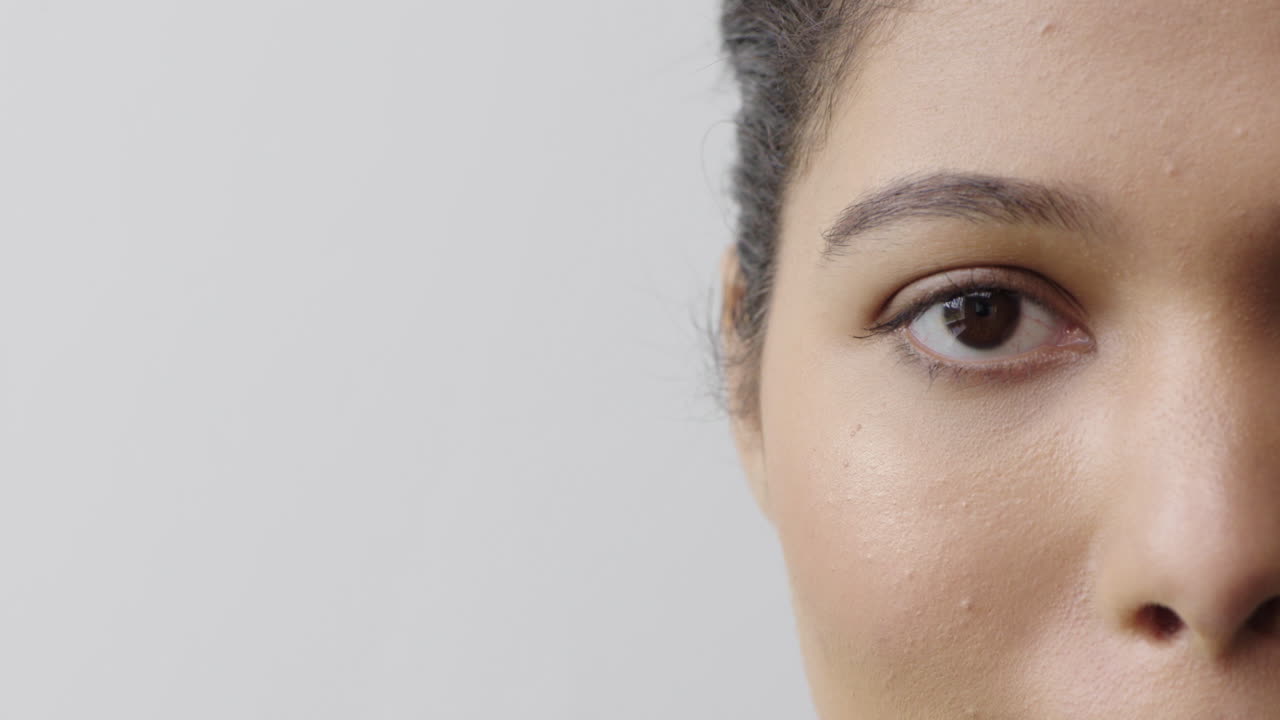 cerca de la mujer hispana ojo mirando a la cámara parpadeando mitad de la cara aislada en fondo blanco copia espacio concepto de cuidado de la piel