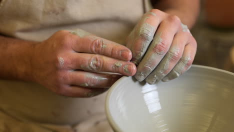 potter gently forming handmade edge of ceramic vessel spinning on pottery wheel