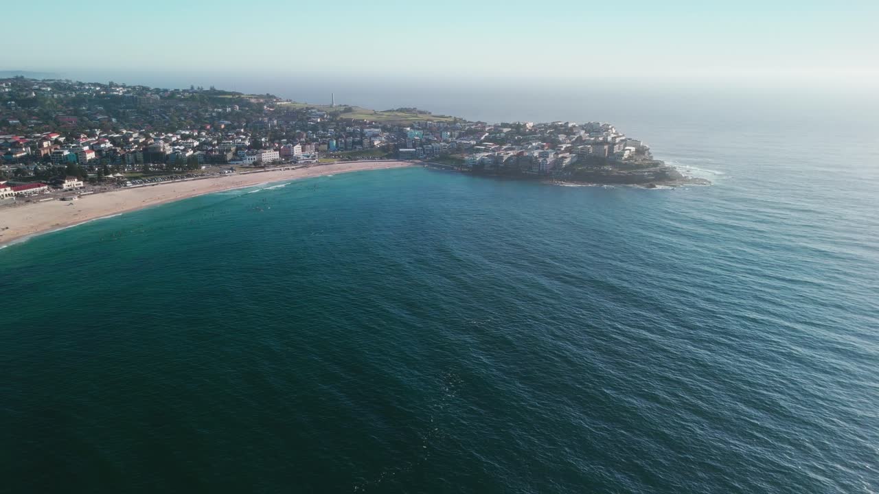 amplias imágenes aéreas de drones capturando la playa de bondi, sus arenas doradas y el pintoresco promontorio costero bajo cielos azules claros. capturado en 4k a 25 fps, mostrando la icónica costa de sídney.