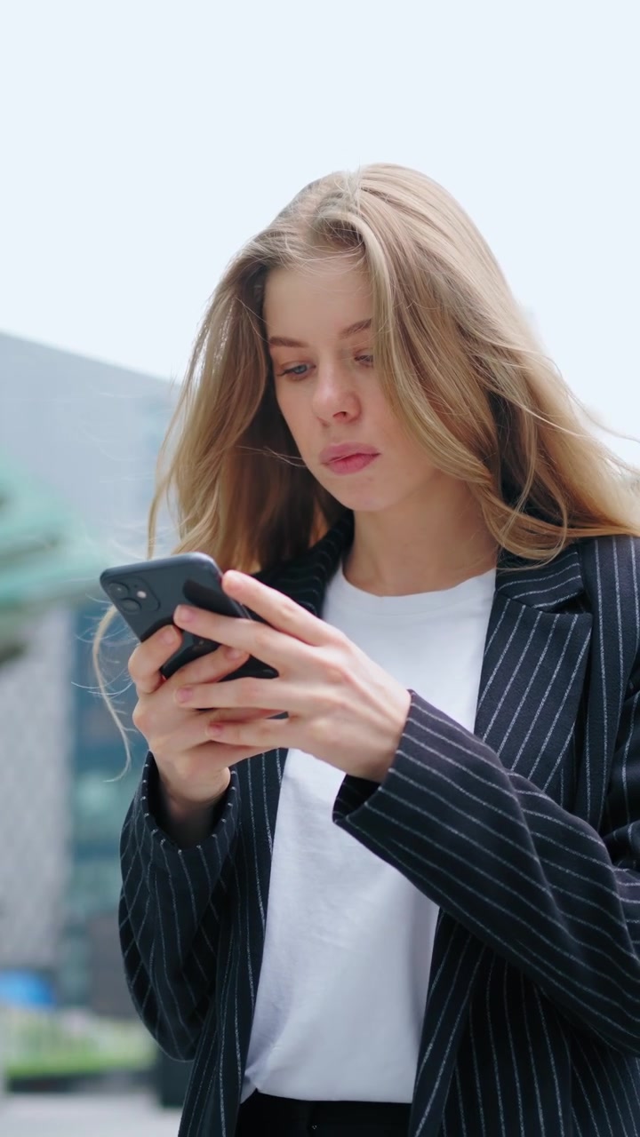 Giovane donna d'affari che usa lo smartphone all'esterno di un moderno palazzo per uffici