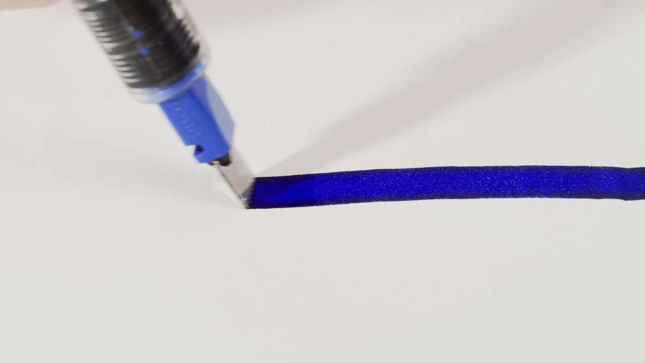 Primo piano di una penna calligrafica che disegna una linea blu su carta bianca
