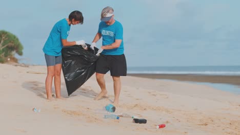 young caucasian man and woman cleaning up plastic garbage from beach