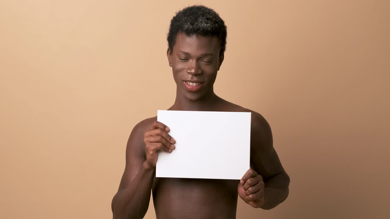 Cheerful african black person shirtless holding blank poster for presentation over beige background