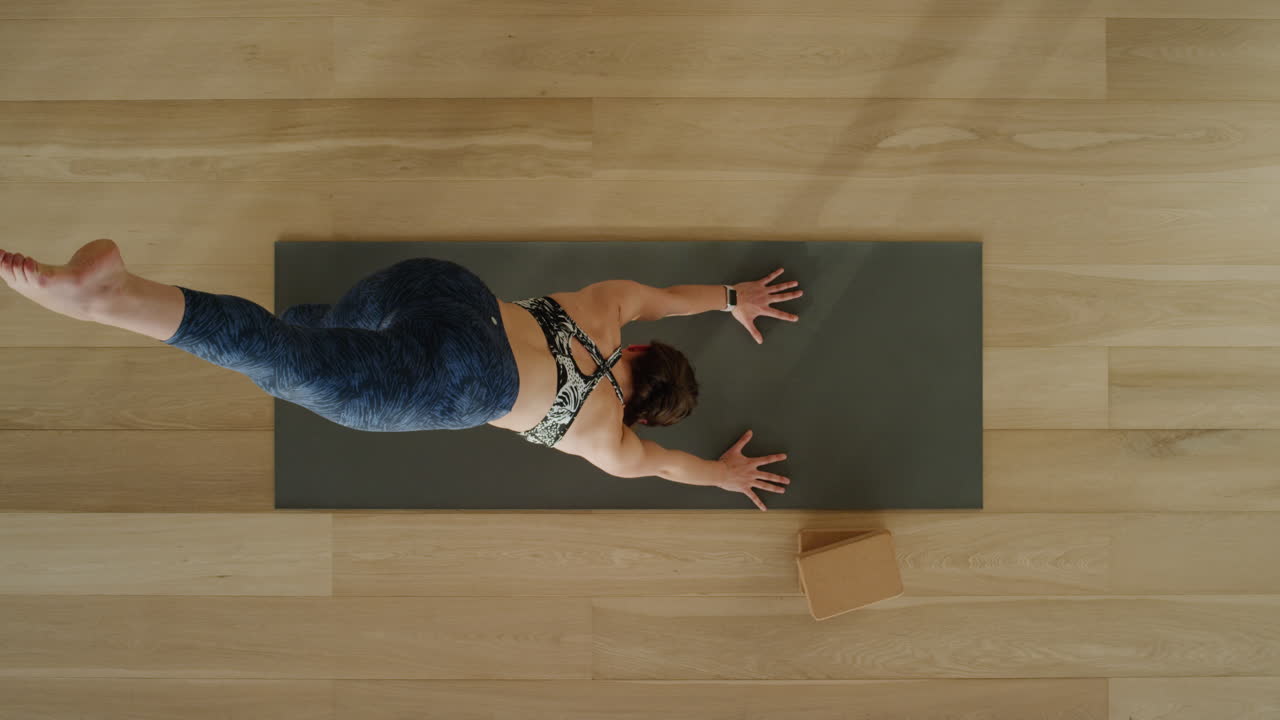 vista superior de una mujer de yoga practicando una pose de perro boca abajo de tres patas en un estudio de ejercicios disfrutando de un estilo de vida saludable practicando meditación en una colchoneta de ejercicios