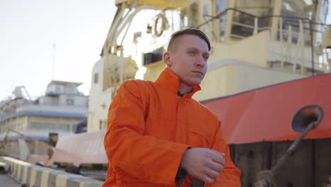 Dock-worker-in-orange-uniform-sitting-in-the-harbor-and-telling-something-to-his-fellow-workers-in-the-port